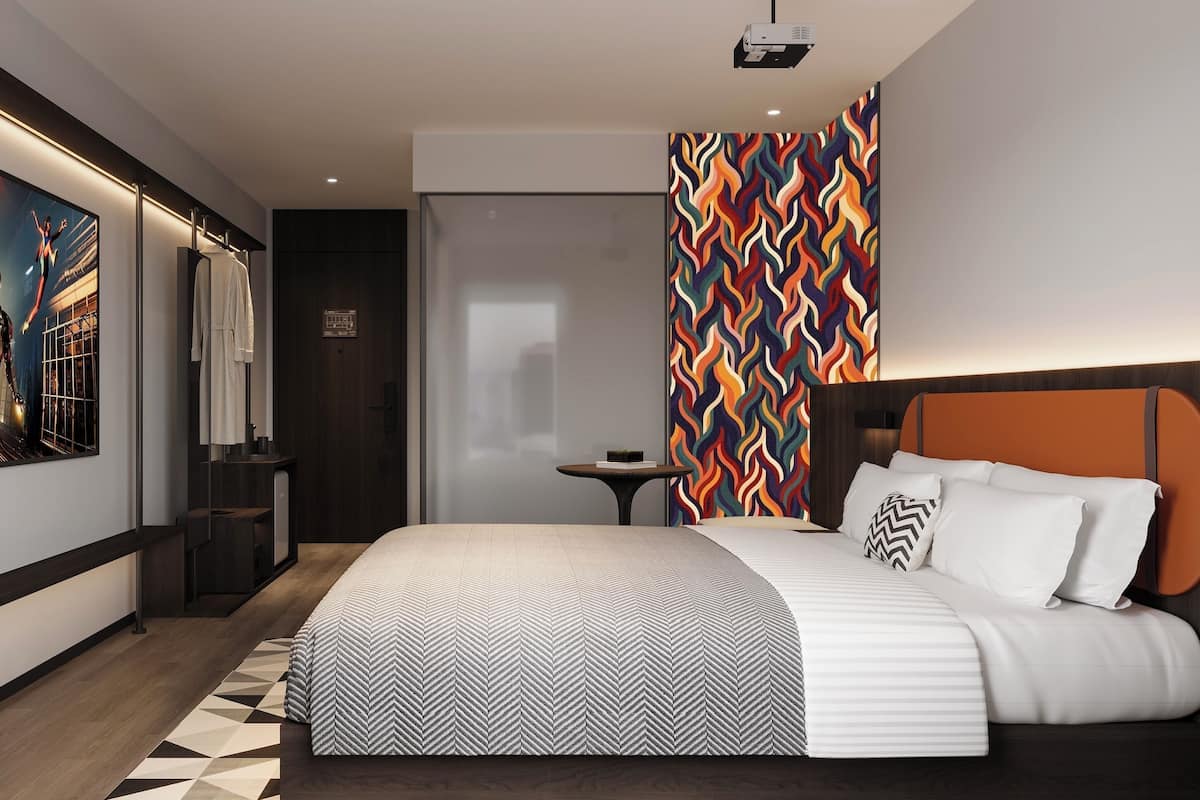 A modern hotel room with a large bed, a projector, a vibrant wall mural, and a geometric-patterned rug.
