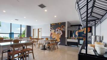 Uma sala de jantar moderna com mesas e cadeiras, um mural na parede e um balcão de buffet com pratos.