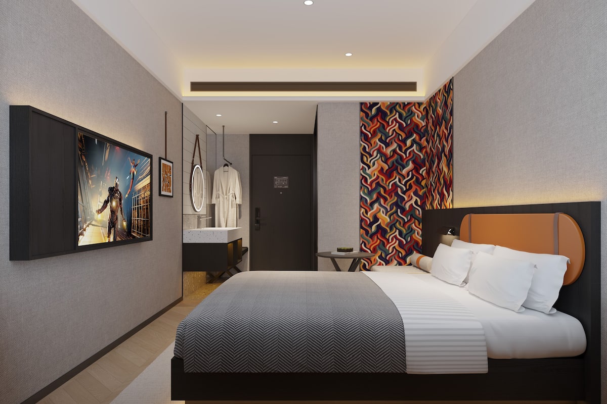 A modern hotel room with a large bed, a bathroom with a mirror, and a TV on the wall.