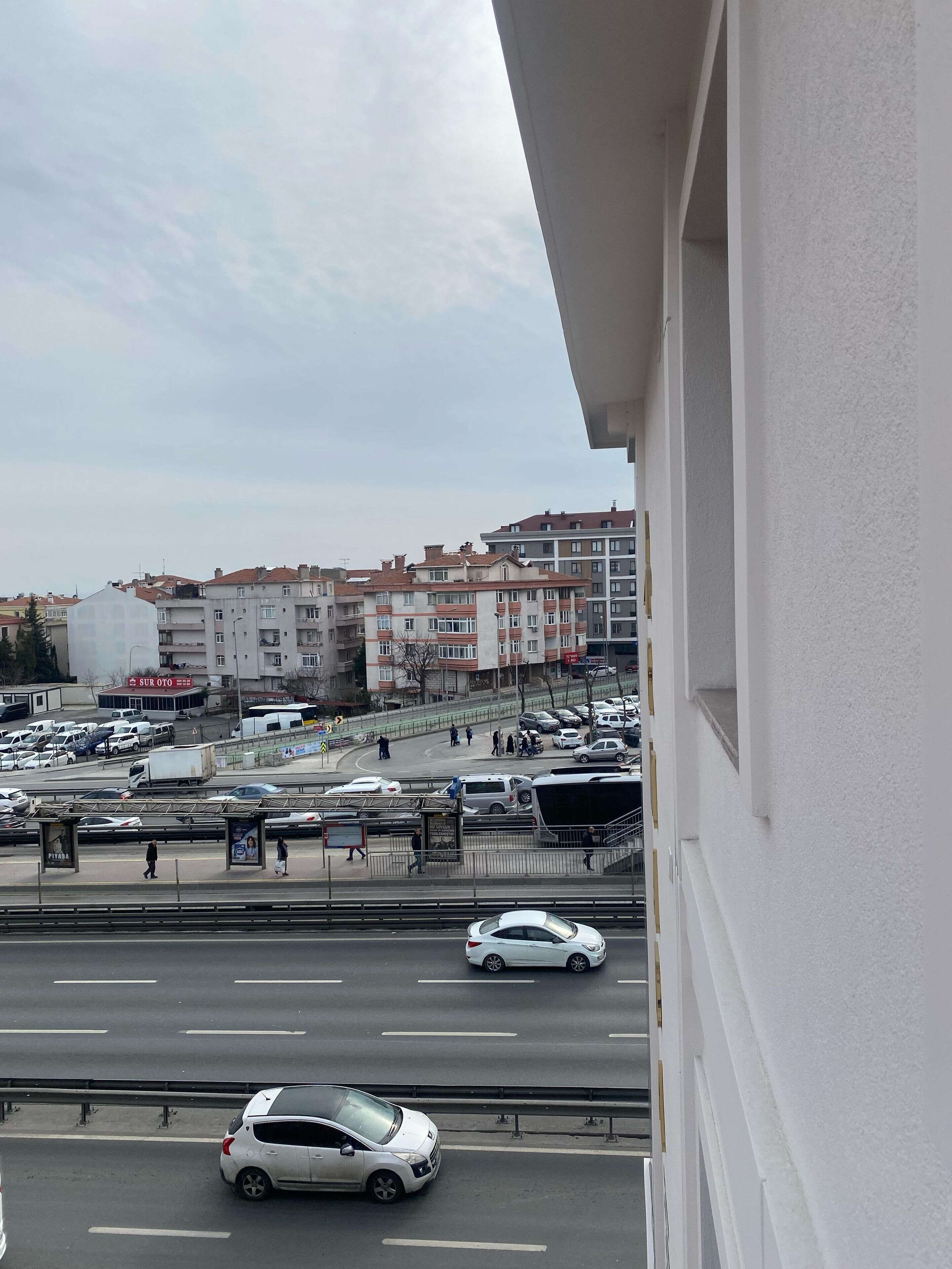 A view of a multi-story building with balconies, a parking lot, and a road with cars.