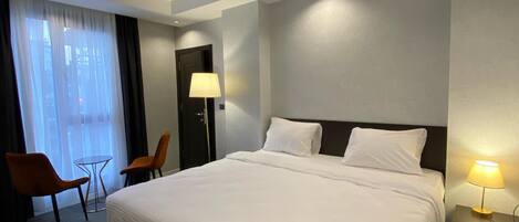 A hotel room with a large bed, two chairs, a small table, and a lamp.