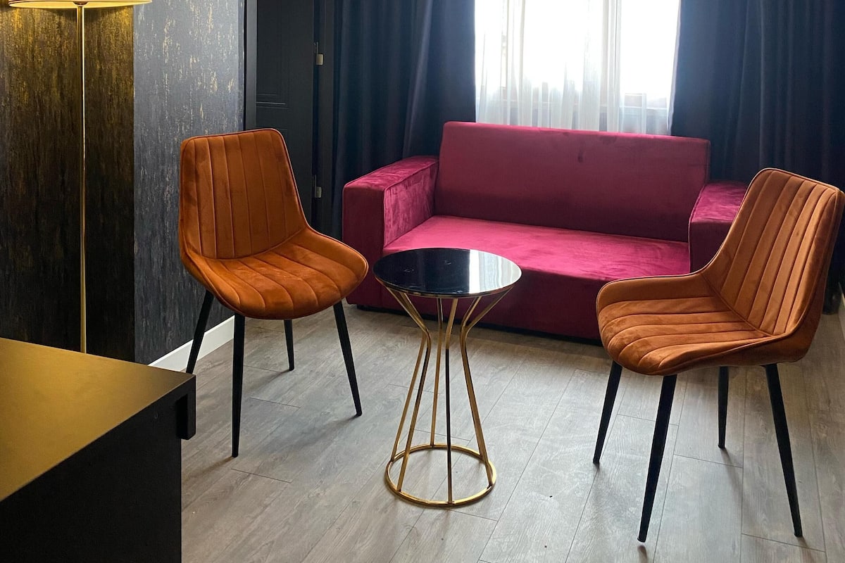 A modern hotel room with a red sofa, two orange chairs, a small round table, and a lamp.
