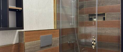 A modern bathroom with a glass-enclosed shower, a white toilet, and a wooden vanity.