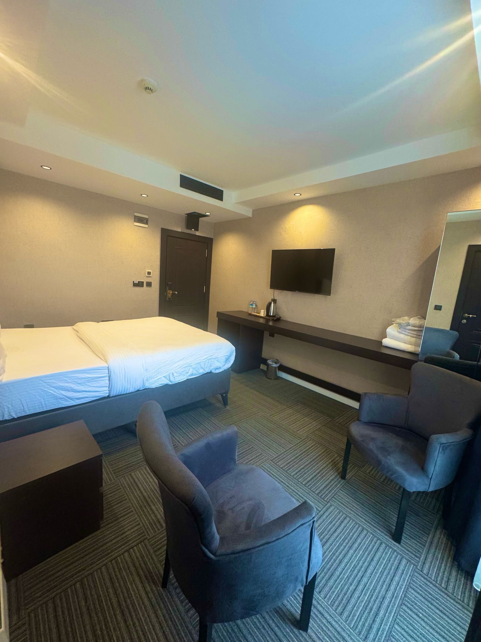 Ein Hotelzimmer mit einem Bett, zwei Sesseln, einem Schreibtisch, einem Flachbildfernseher und einem Spiegel.