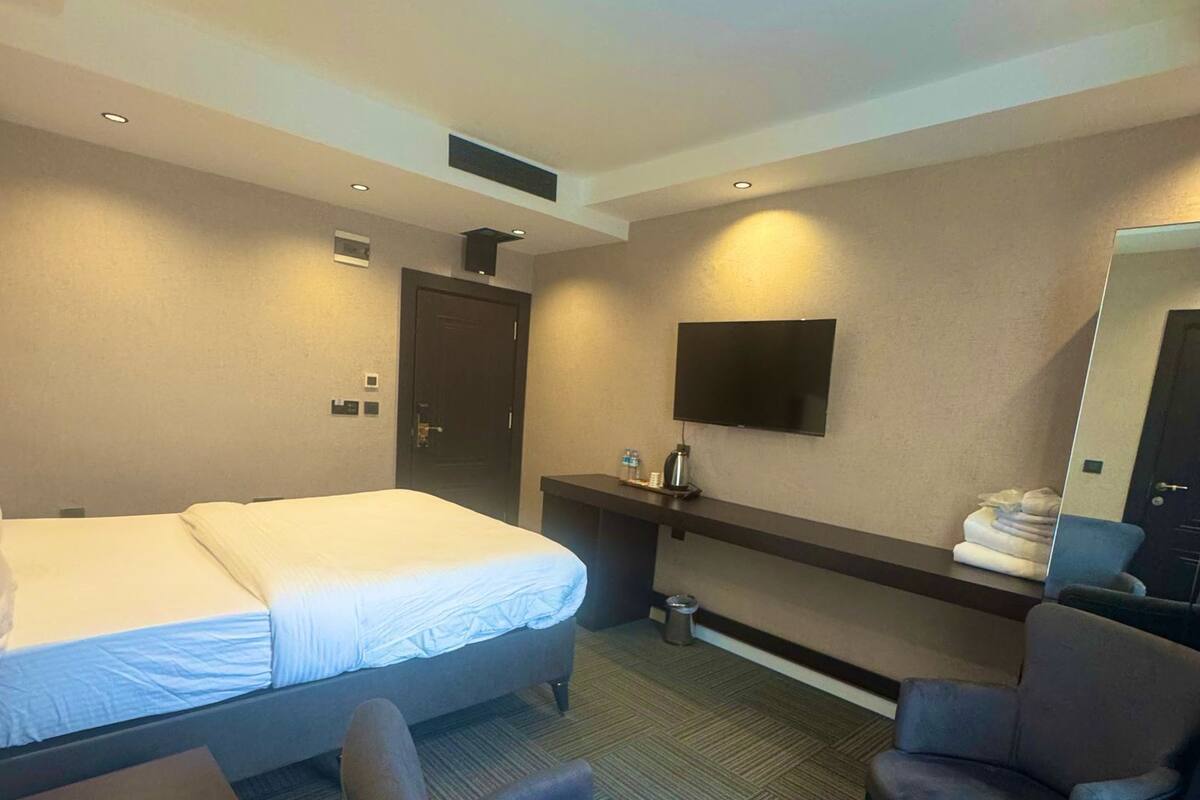 A hotel room with a bed, two armchairs, a desk, a flat-screen TV, and a mirror.