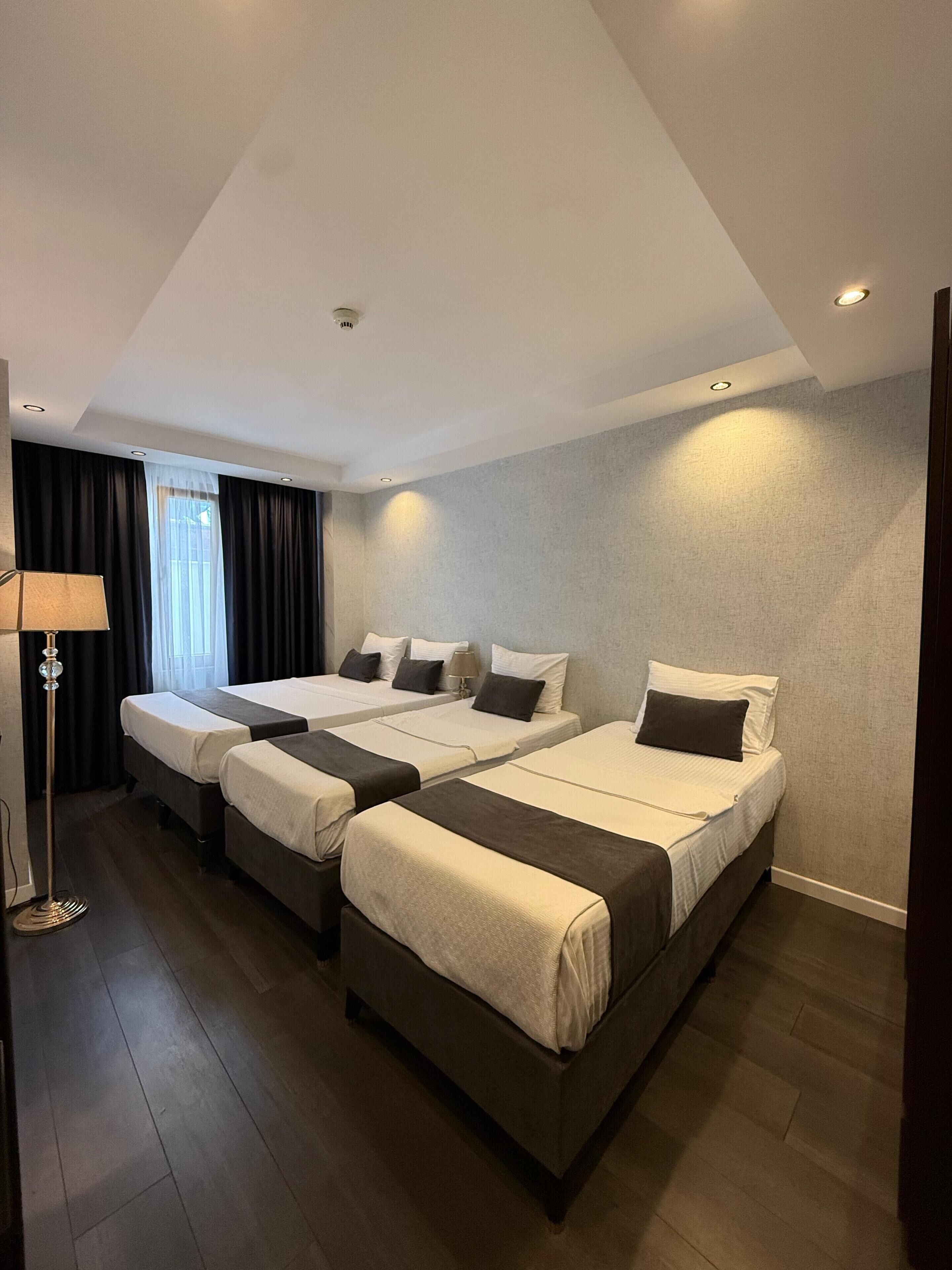 A hotel room with three beds, a floor lamp, and a window with curtains.