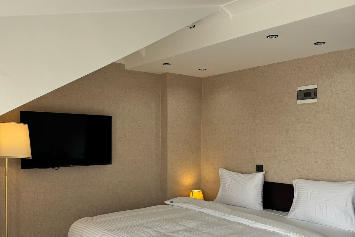 A modern hotel room with a large bed, a flat-screen TV mounted on the wall, and a floor lamp.