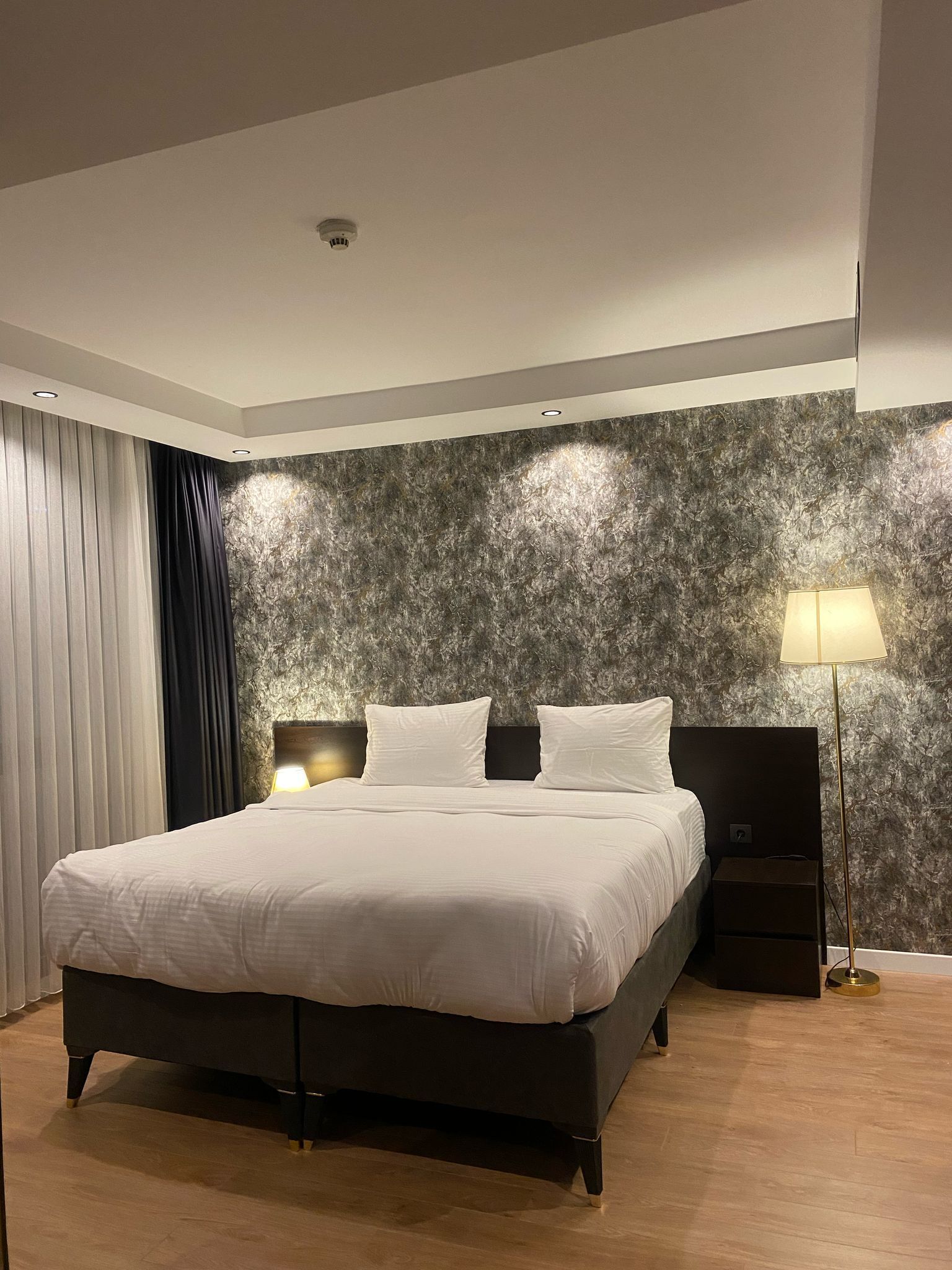 Un dormitorio moderno con una cama grande, cabecera oscura y pared con textura.