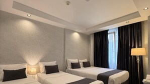 Una habitación de hotel con tres camas, una mesita de noche con lámpara y una ventana con cortinas.