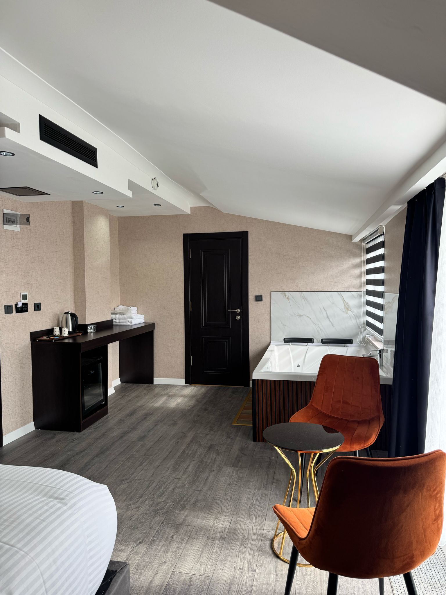 Une chambre d’hôtel moderne équipée d’un lit, d’un bureau avec une bouilloire, d’une chaise, d’une petite table et d’une fenêtre avec des rideaux.