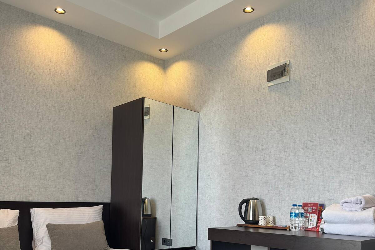 A modern hotel room with a large bed, a desk, a mirror, and a small trash bin.