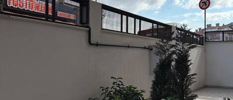 A rooftop terrace with potted plants, a metal railing, and a view of a building with a 'DUR' sign.