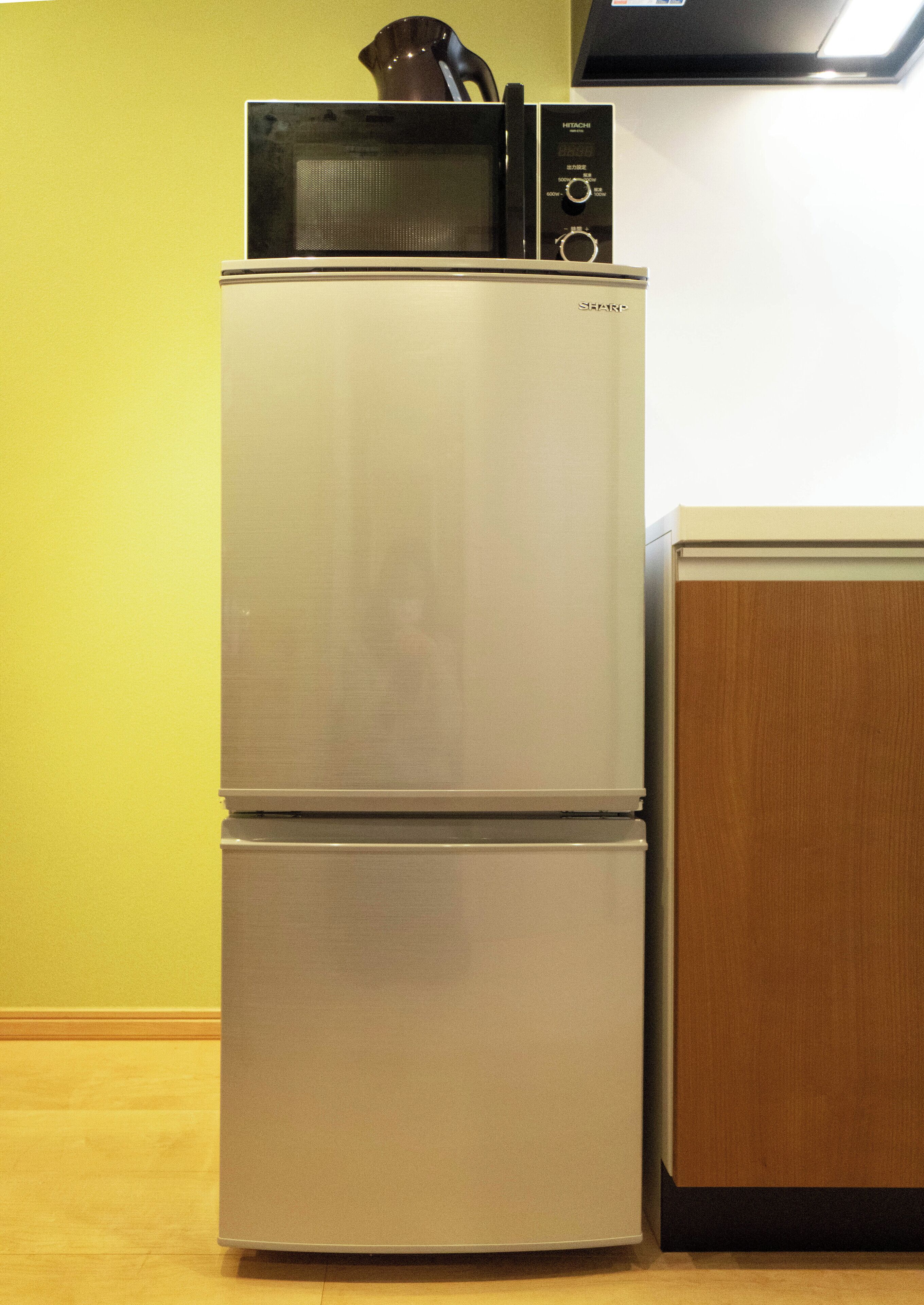 A stainless steel refrigerator with a microwave on top, next to a wooden cabinet.