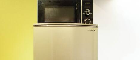A stainless steel refrigerator with a microwave on top, next to a wooden cabinet.