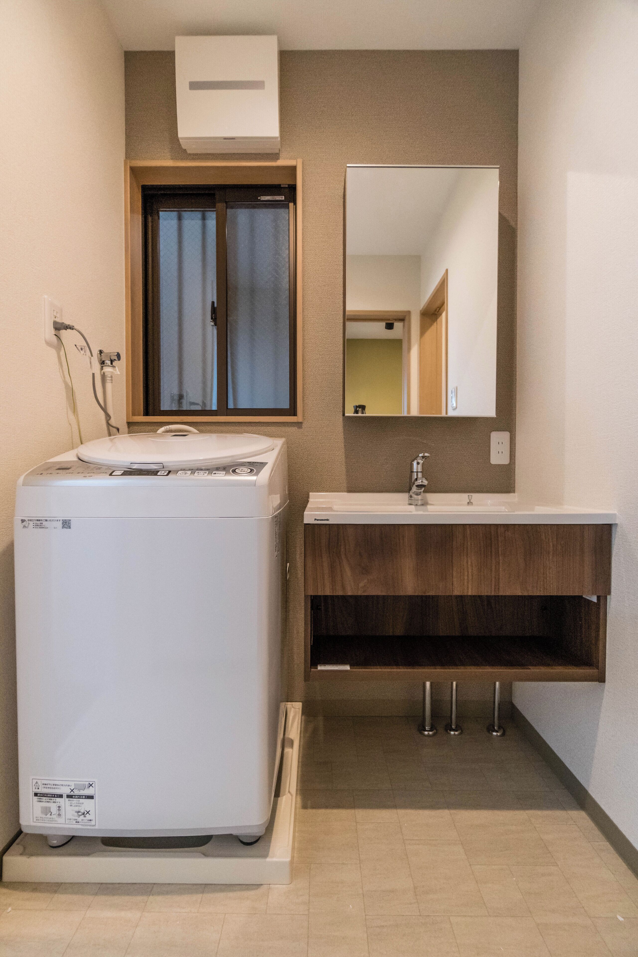 Un baño pequeño con lavadora incorporada, tocador de madera, espejo y ventana con cortinas.