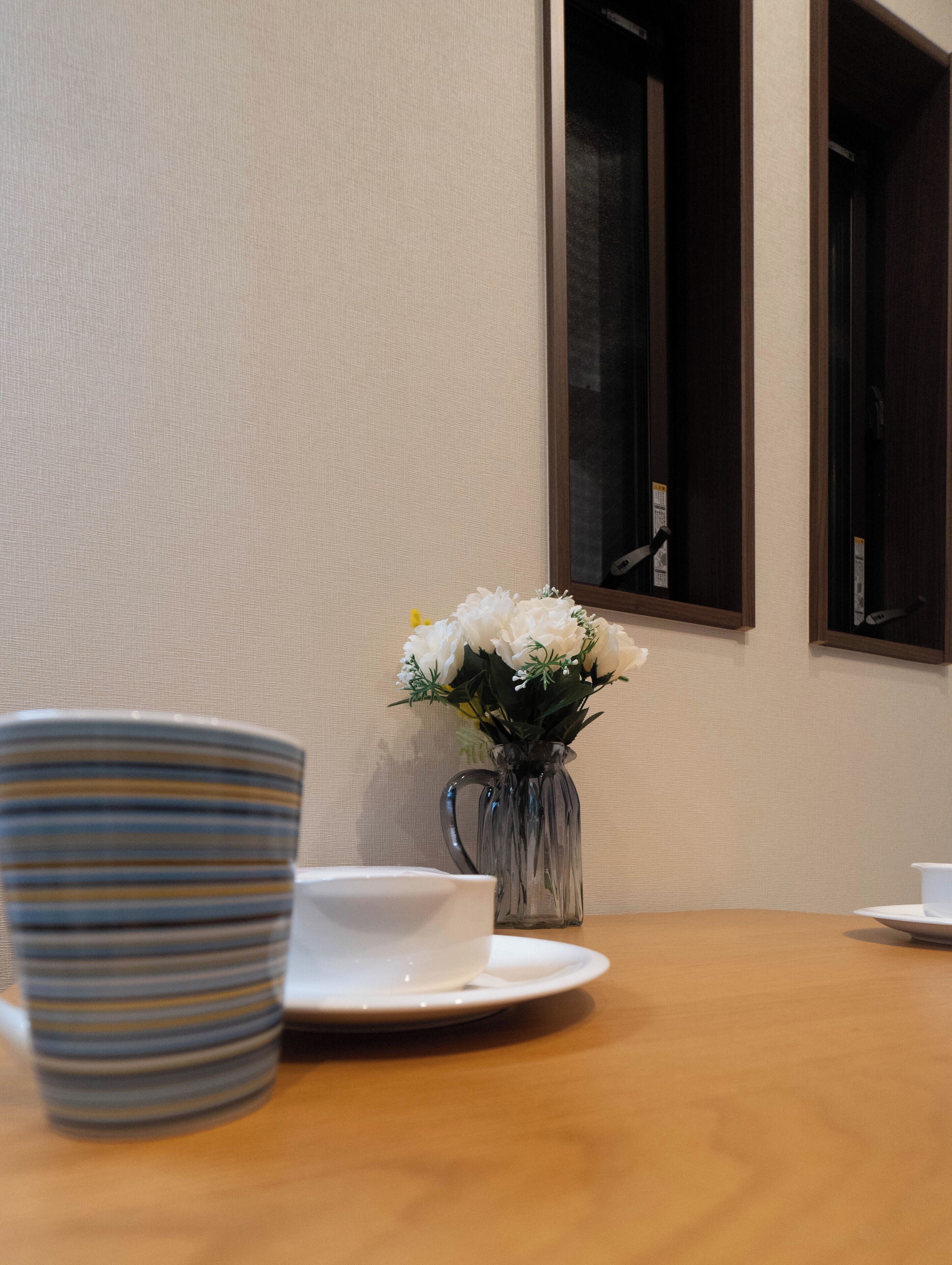 A dining table with a striped bowl, a white cup, and a vase with white flowers.