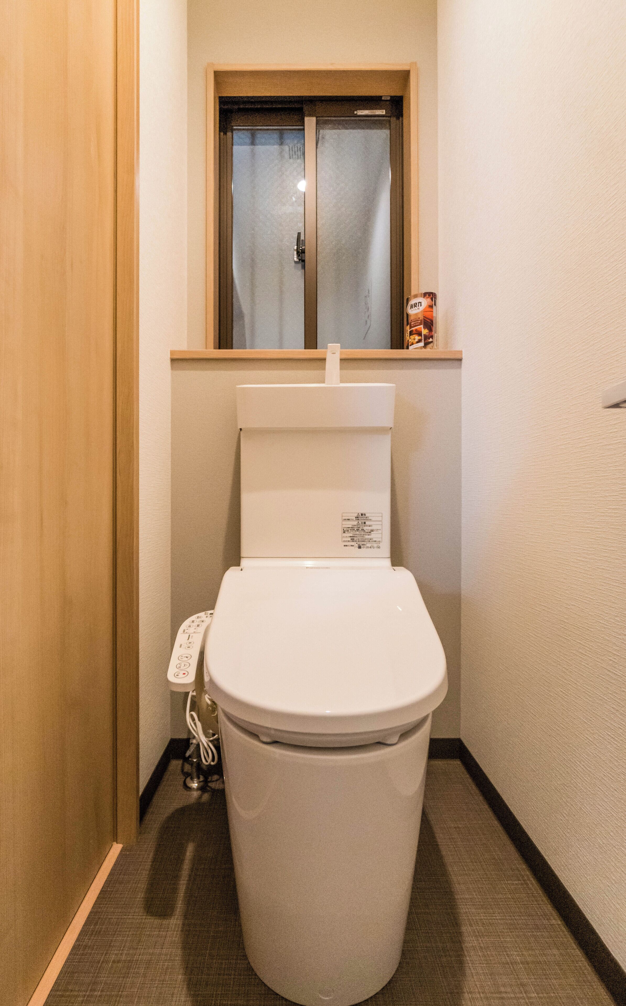 Een kleine badkamer met toilet, een klein raam en een stopcontact op de muur.