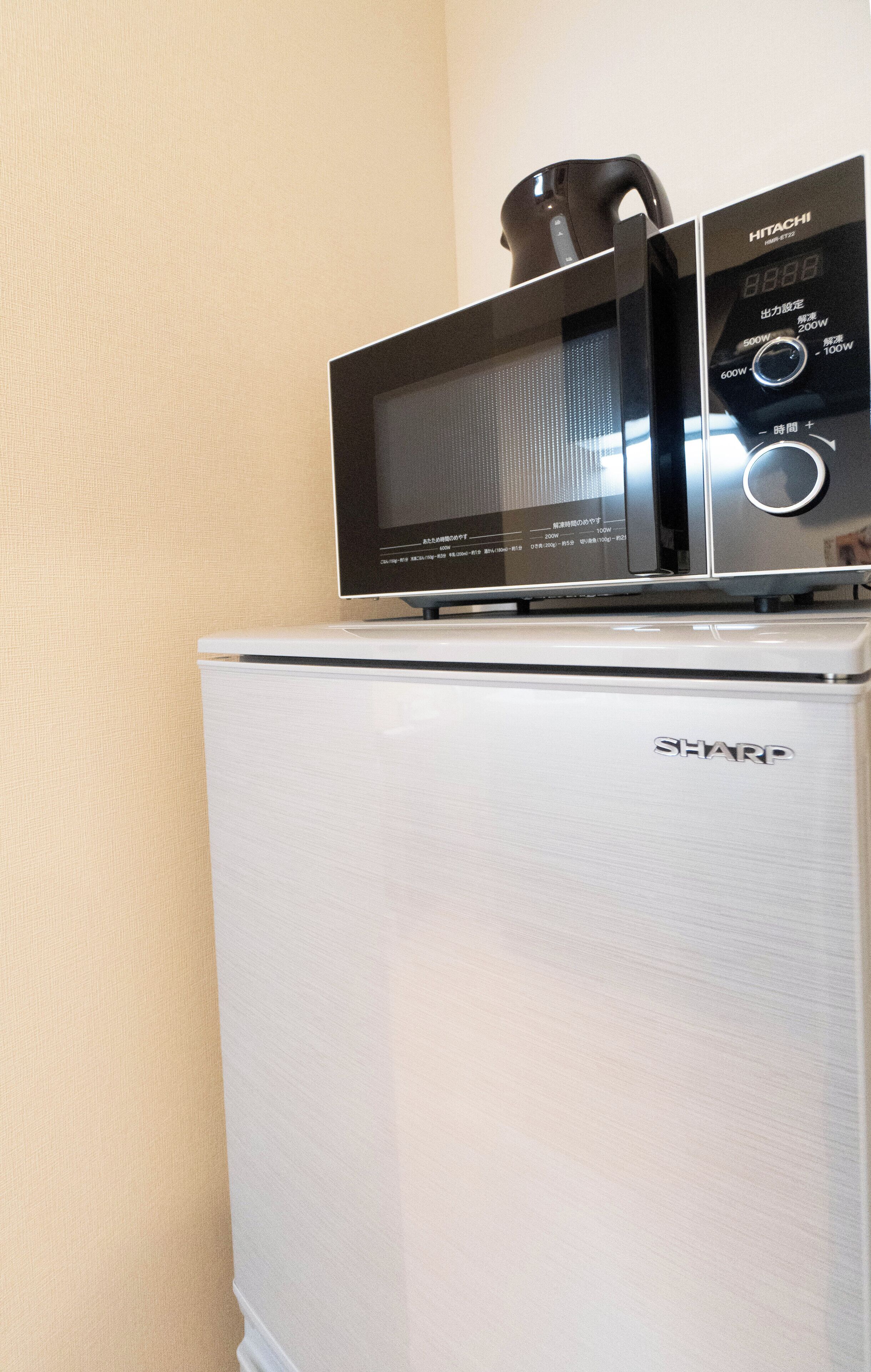 Un réfrigérateur blanc de la marque Sharp, surmonté d’un four à micro-ondes Hitachi.