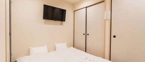 A hotel room with a bed, a television mounted on the wall, and a sliding door closet.