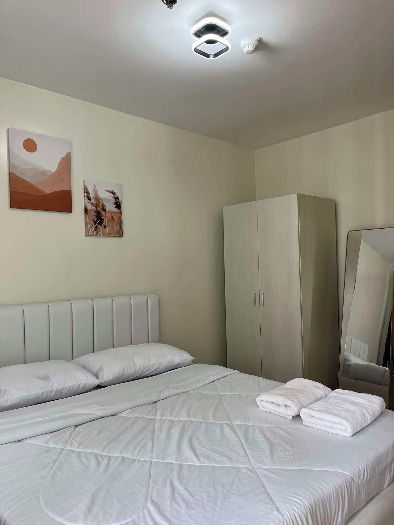 A neatly made bed with white linens, a large wardrobe, and a wall-mounted artwork depicting a desert scene.