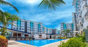 A modern hotel with a swimming pool, multiple balconies, and a clear blue sky.