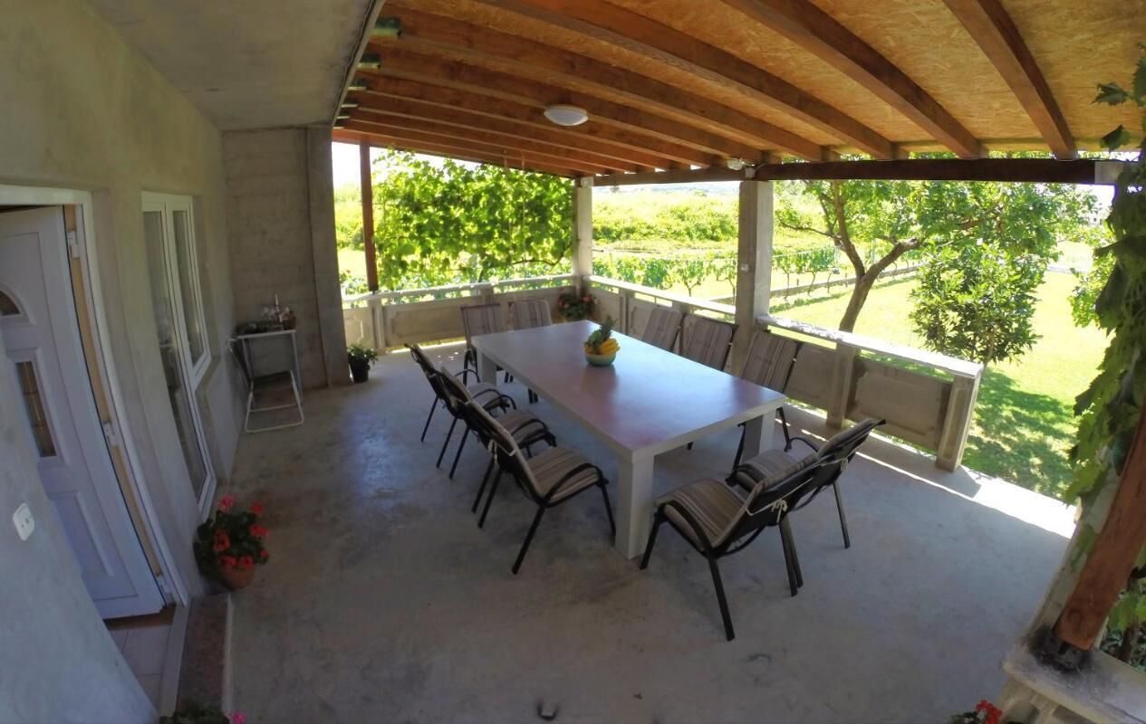 A covered patio with a table and chairs, a view of a vineyard, and a door to the left.