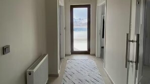 A hallway with a radiator, a patterned rug, and a door leading to a balcony. - Alacaatlı Suit (Ankara)