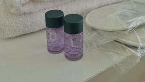 A neatly folded white towel stacked on a white surface, two bottles of shampoo, and a plastic-wrapped item. - Alacaatlı Suit (Ankara)
