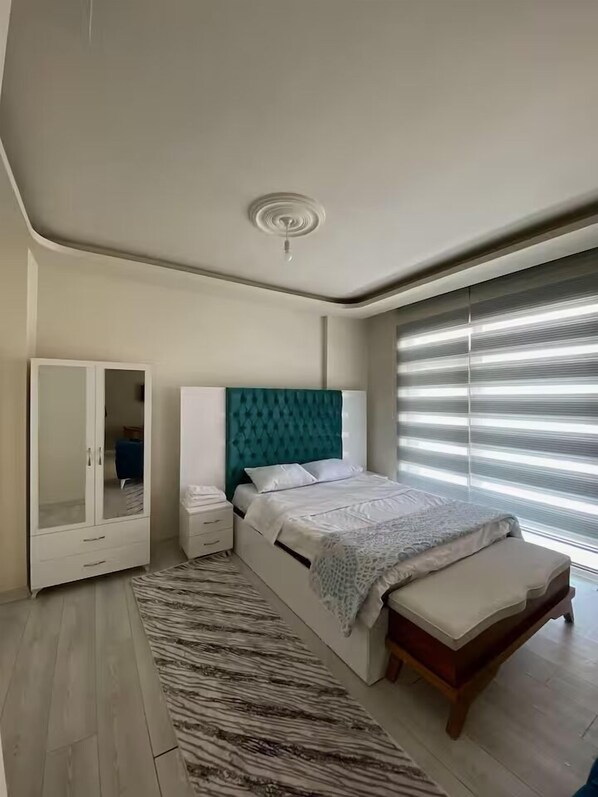 A bedroom with a bed, a wardrobe, a bedside table, and a window with blinds. - Alacaatlı Suit (Ankara)