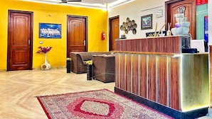 A reception area with a wooden reception desk, two sofas, a patterned rug, and a ceiling fan. - GoBravo 842 Rejoice Hotel Gurgaon (Gurugram)