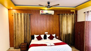 A bedroom with a bed, an air conditioning unit, a ceiling fan, wooden panel walls, and a wardrobe. - GoBravo 842 Rejoice Hotel Gurgaon (Gurugram)