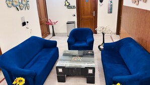 A room with two blue sofas, a glass coffee table, and a wooden door marked with the number 211. - GoBravo 842 Rejoice Hotel Gurgaon (Gurugram)