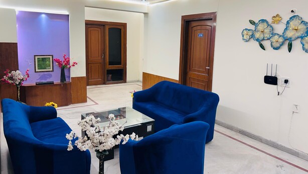A hotel lobby with blue armchairs, a reception desk, a wall-mounted flower decoration, and a ceiling fan. - GoBravo 842 Rejoice Hotel Gurgaon (Gurugram)