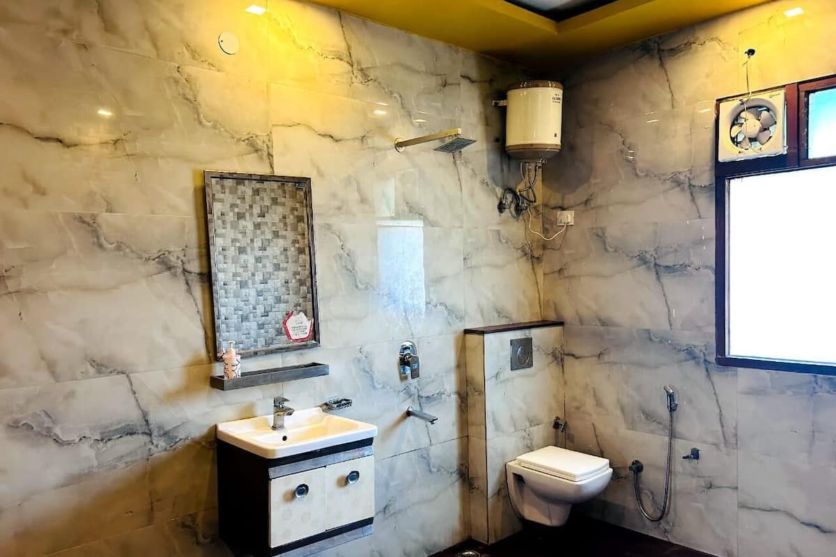 A bathroom with marble walls, a white sink, a toilet, and a shower.