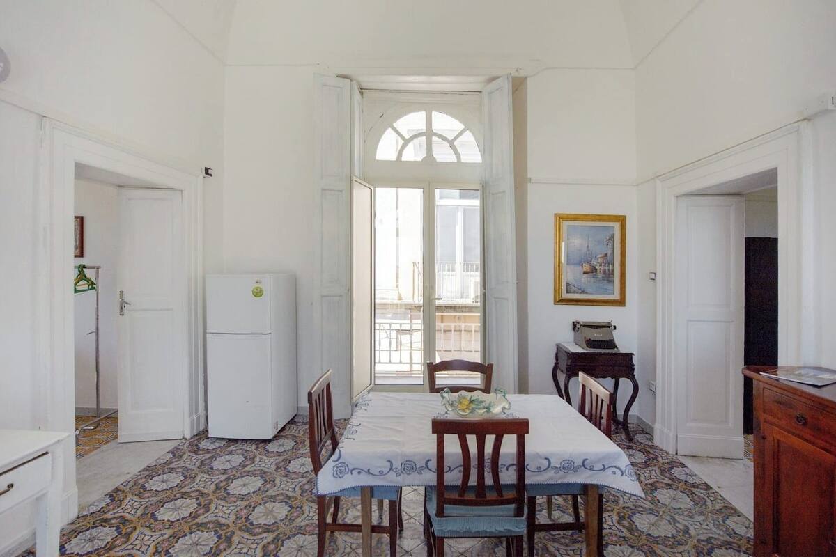 A dining area with a table set for four, a refrigerator, a typewriter, and a painting on the wall.