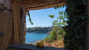 Une fenêtre rustique en pierre offrant une vue sur un paysage côtier, comprenant une étendue d’eau et des bateaux.
