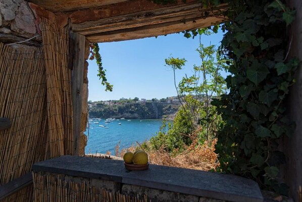 A rustic stone window with a view of a coastal landscape, including a body of water and boats.