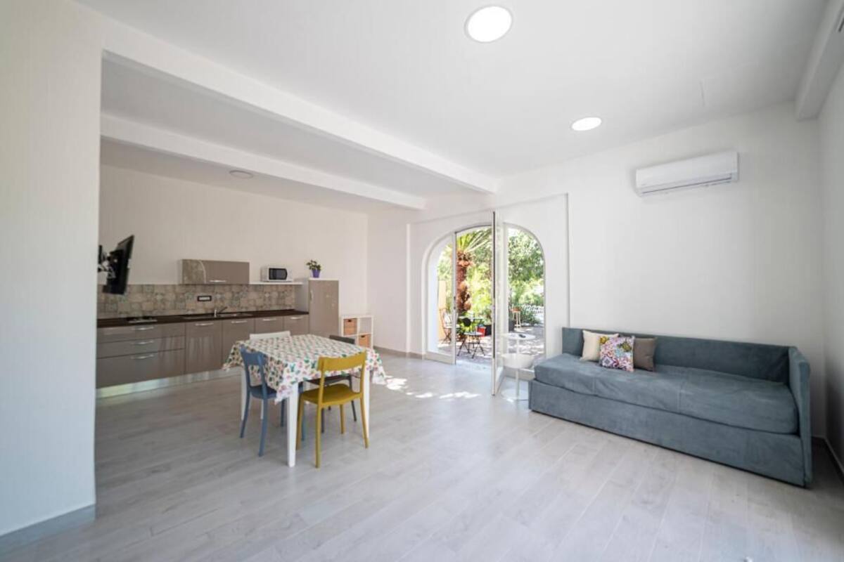 A spacious living area with a dining table and chairs, a grey sofa, and a kitchen in the background.