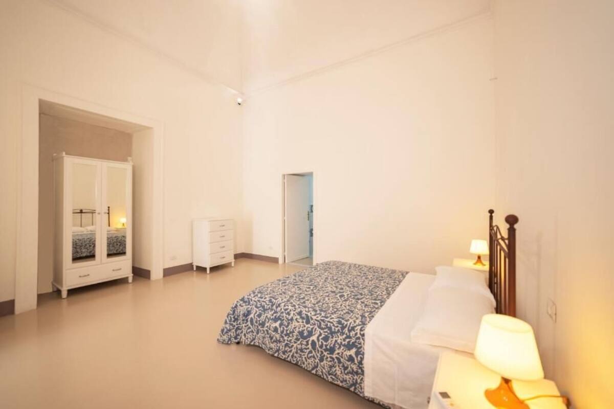 A bedroom with a bed, bedside table, lamp, wardrobe, and a door.