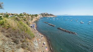 Une plage côtière bordée d’un rivage rocheux, avec une mer d’un bleu limpide et un bâtiment historique perché sur une colline.