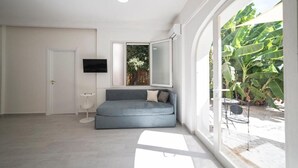 Un salon moderne avec un canapé gris, une petite table blanche et une grande fenêtre donnant sur un paysage verdoyant.