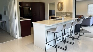A modern kitchen with a central island, bar stools, dark cabinets, and a large mirror. - Paradise Shores Ruakaka Beach 600m Walk to the Beach (Ruakaka)