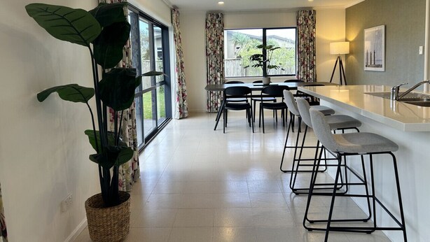 A modern kitchen with a bar area, large windows, and a potted plant. - Paradise Shores Ruakaka Beach 600m Walk to the Beach (Ruakaka)