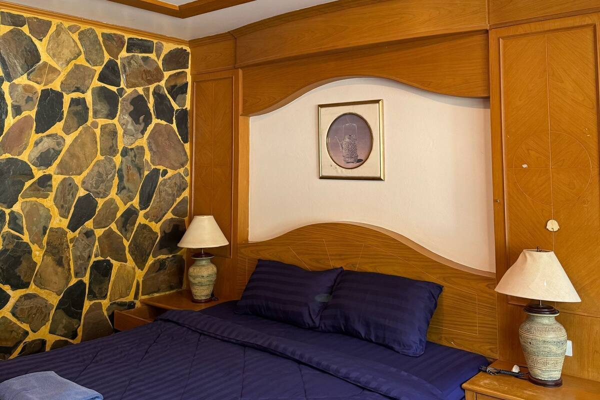 Camera da letto con parete in pietra, testiera in legno, un letto con biancheria azzurra, due comodini con lampade e un quadro appeso al muro.
