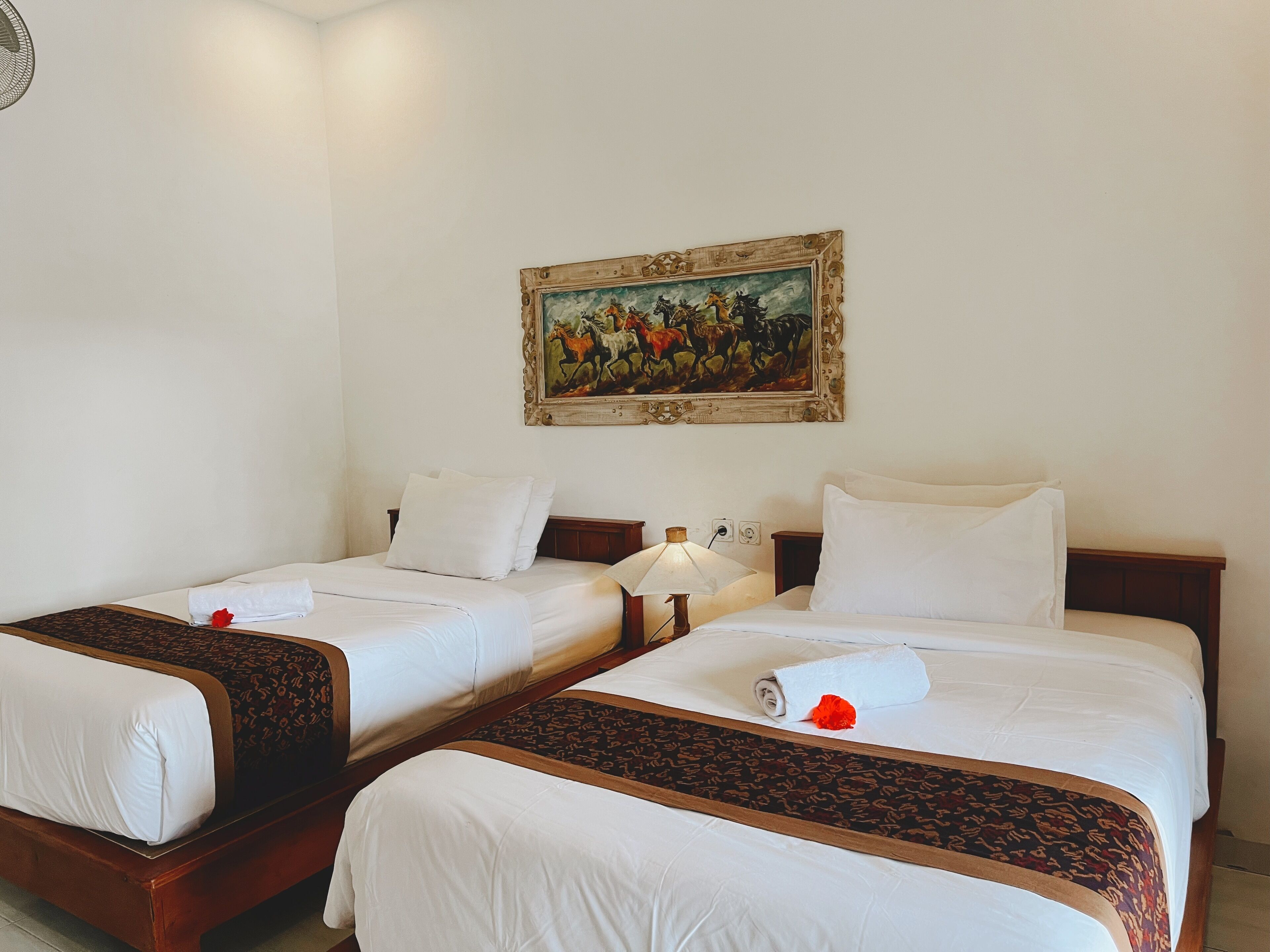 Quarto de hotel com duas camas de solteiro, um quadro na parede e uma mesa de cabeceira com abajur.