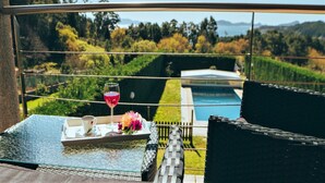 A balcony with a glass table, wicker furniture, a tray with a cup and flowers, and a view of a pool and greenery. - Apartment in Cangas near Playa de Barra (Cangas do Morrazo)
