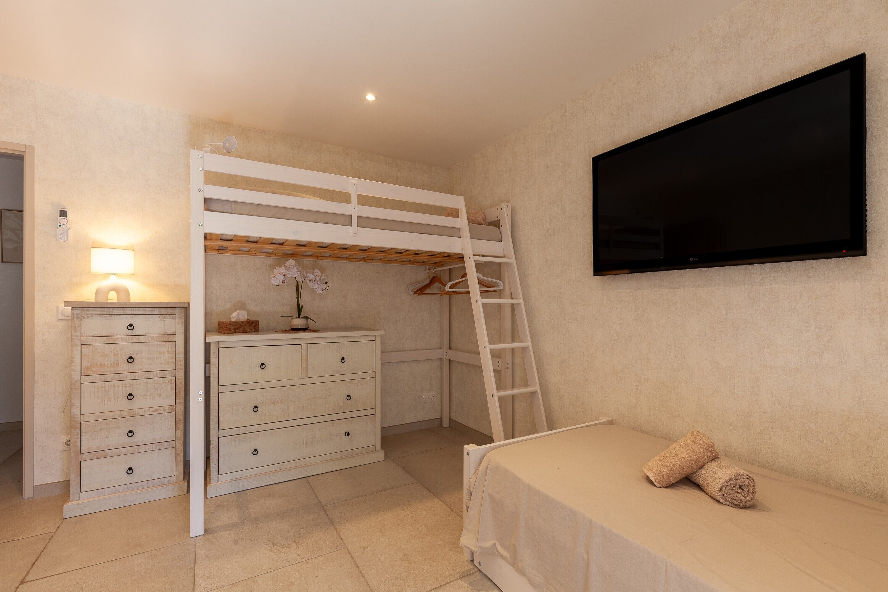 Ein Schlafzimmer mit Etagenbett, Fernseher, Kommode und Nachttisch.