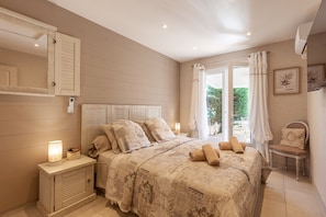 Un dormitorio con cama, mesitas de noche, una silla, una ventana con cortinas y un aire acondicionado de pared.