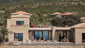 A stone villa with a pool, surrounded by mountains and greenery.