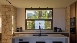 A modern kitchen with a large window, stone walls, and a central island with stools.